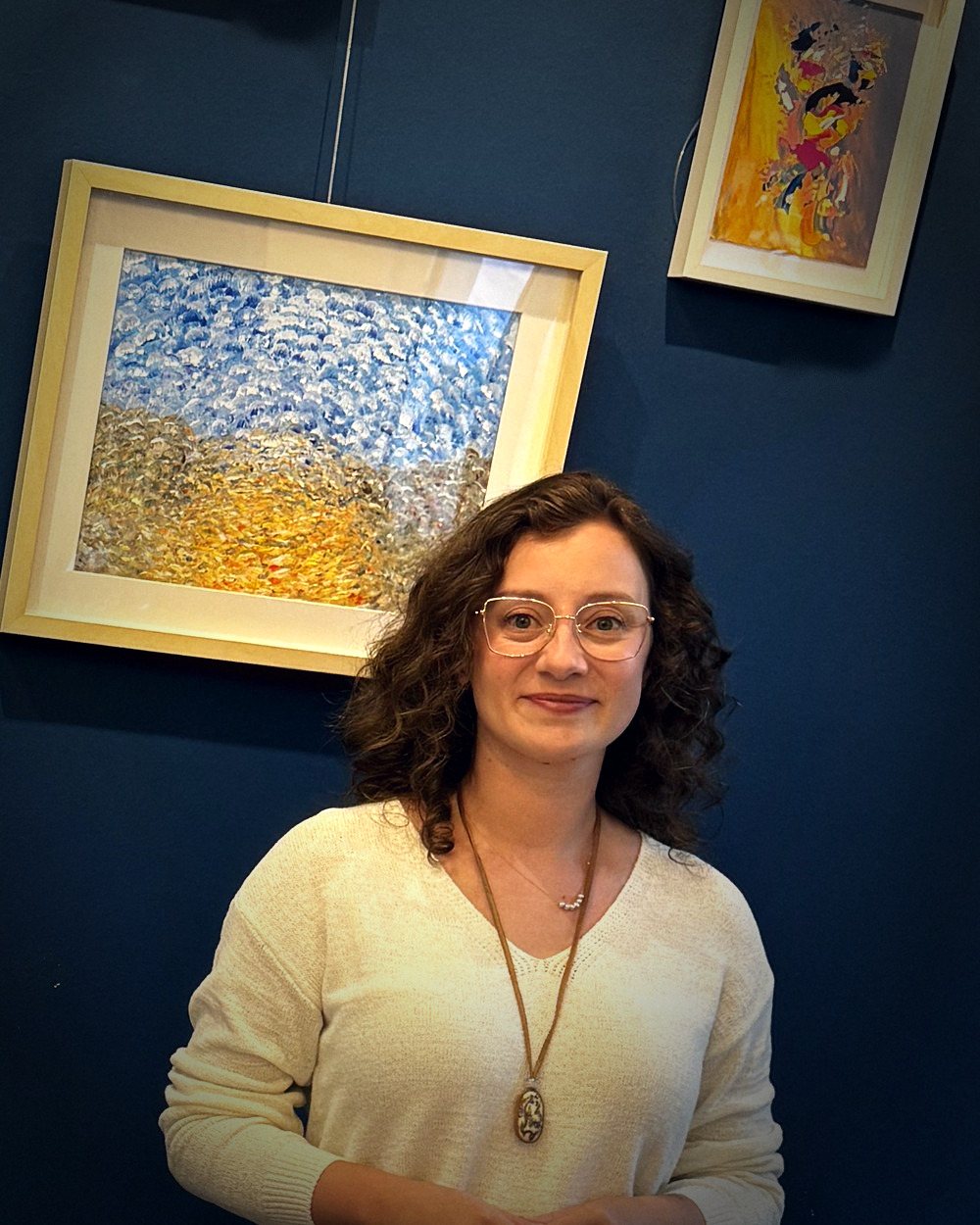 Cansu Öter smiling in a gallery, standing in front of framed paintings.